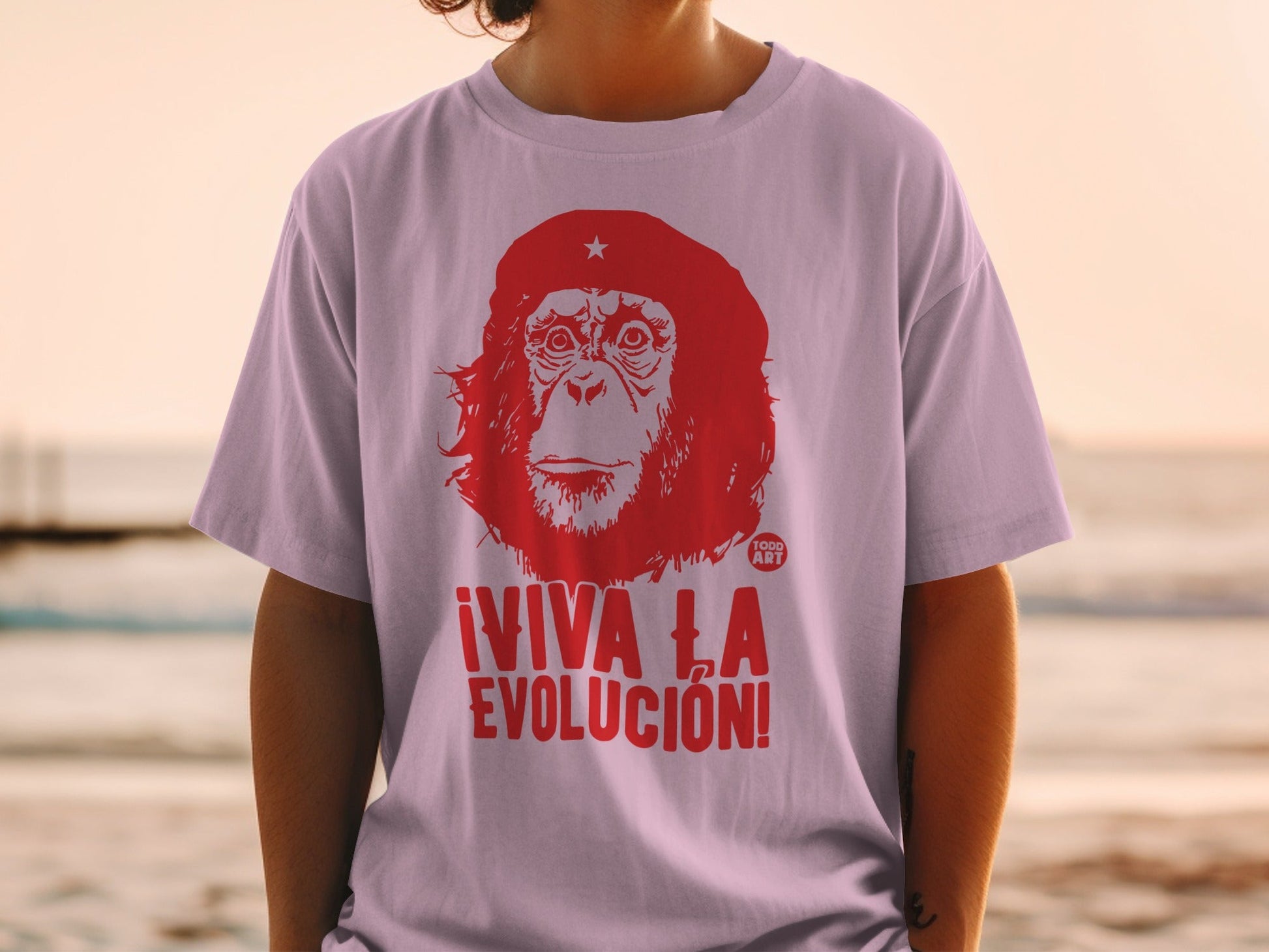 Red primate graphic with ¬°VIVA LA EVOLUCI√ìN! text on a light purple t-shirt.