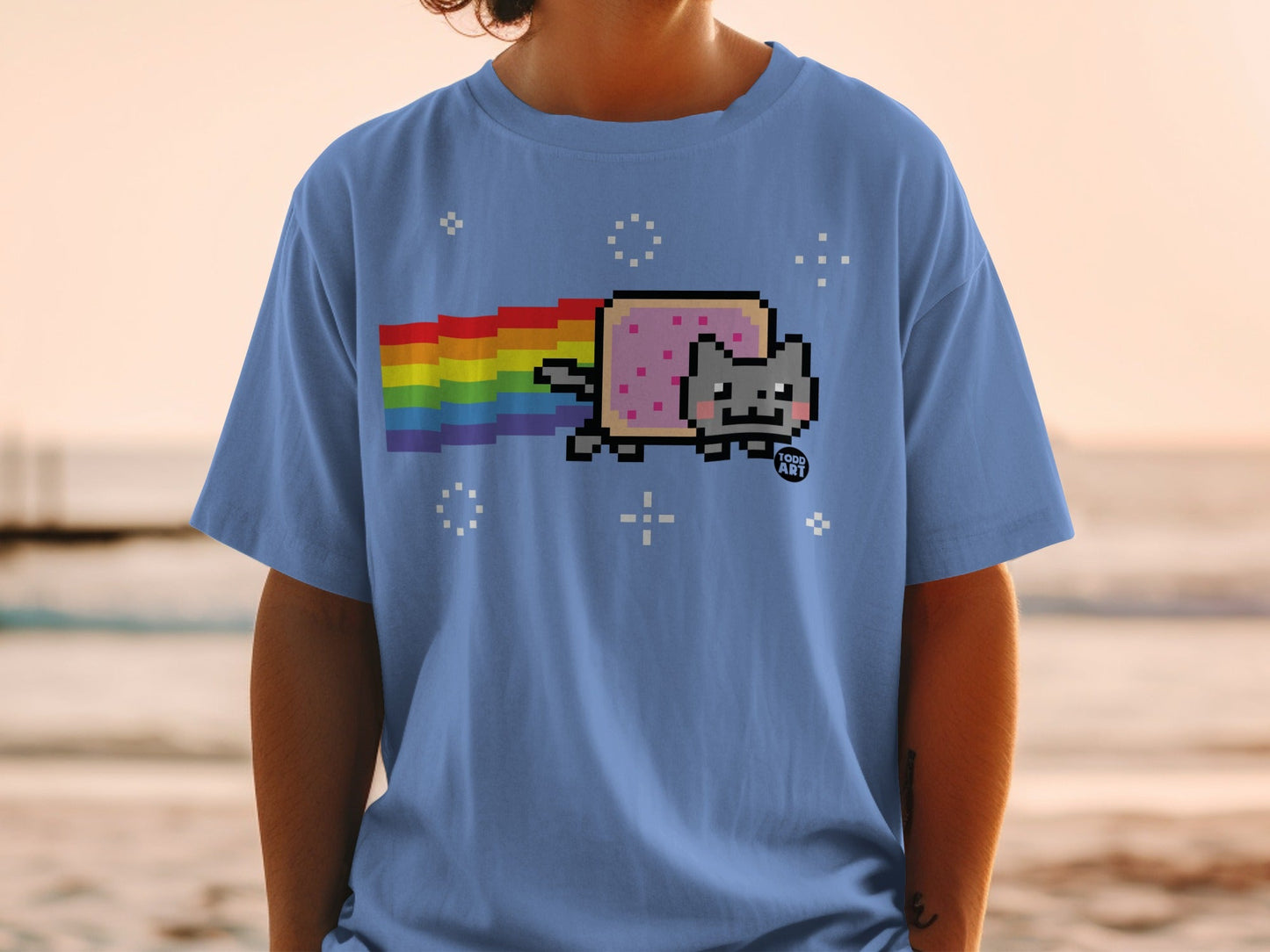 Pixelated cat with rainbow tail on light blue t-shirt.