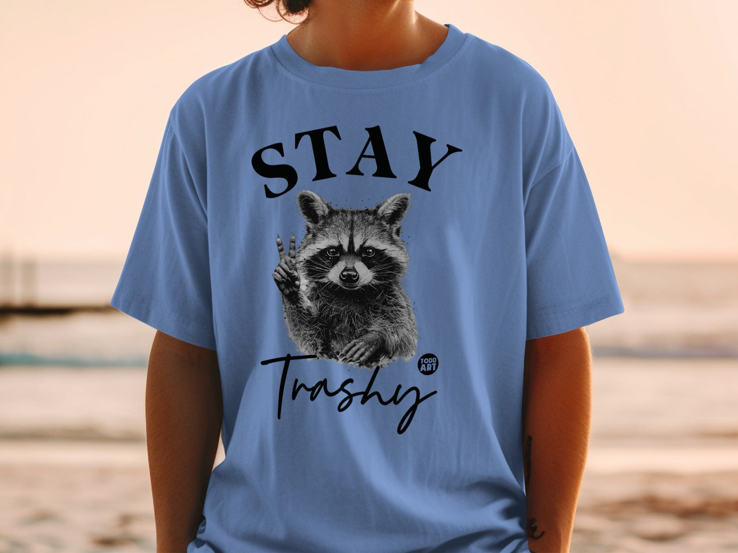 Blue t-shirt with a raccoon holding up peace sign, text "STAY Trashy".