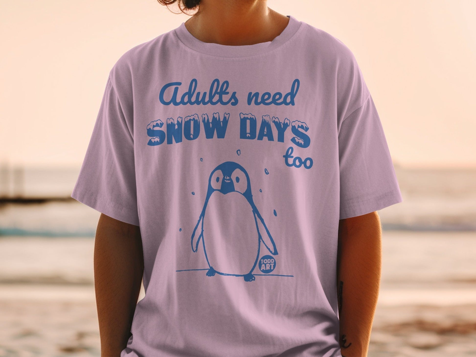 Light purple t-shirt with blue penguin and text "Adults need SNOW DAYS too".