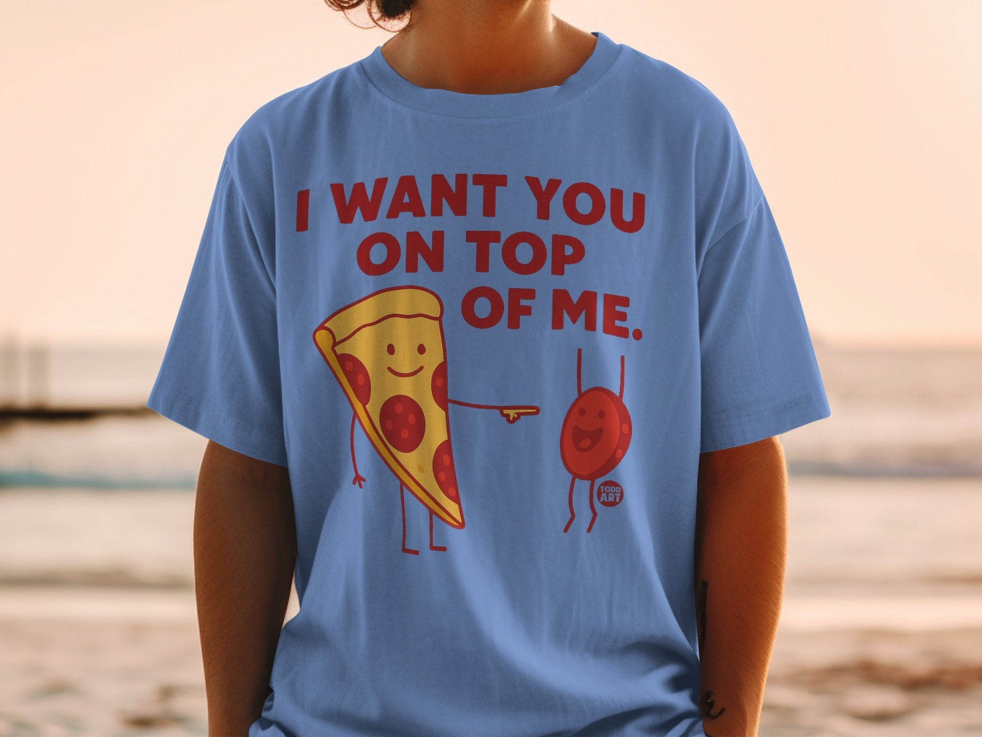 Blue t-shirt with cartoon pizza slice and tomato saying "I WANT YOU ON TOP OF ME."