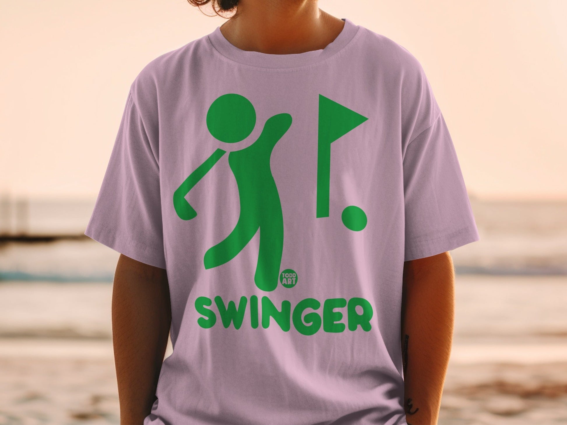 Green golfer swinging, flag, and "SWINGER" text on purple t-shirt.