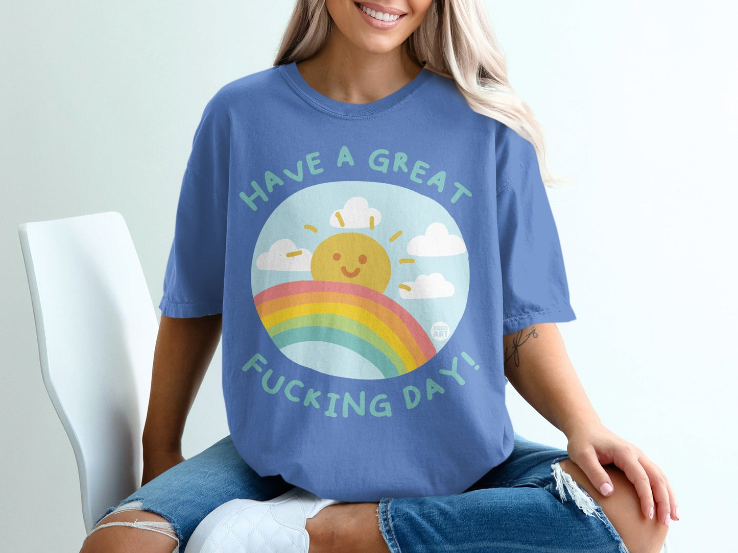 Blue t-shirt with a smiling sun, rainbow, and clouds saying "Have a Great Fucking Day!".