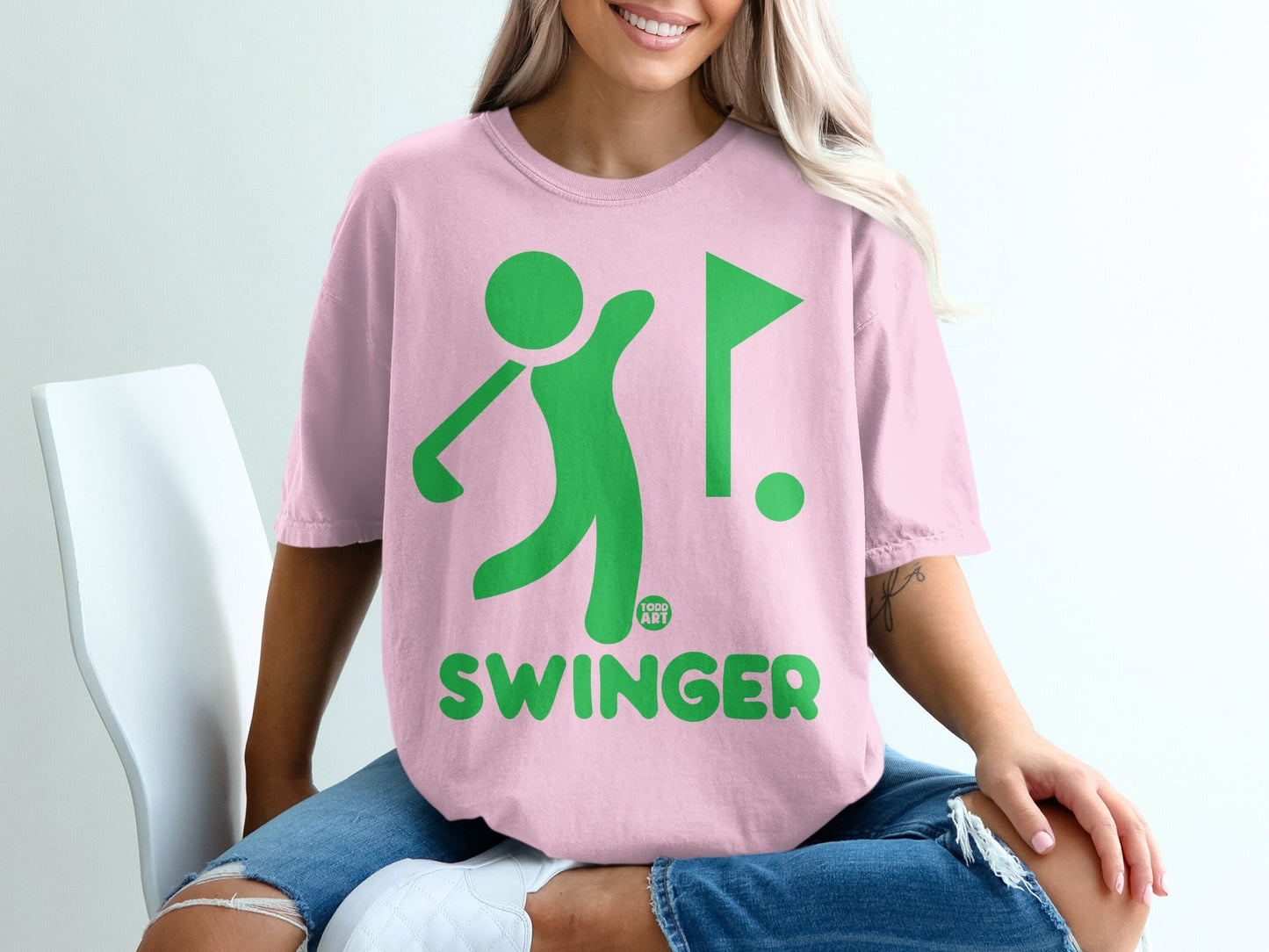 Pink t-shirt with green graphic of a golfer, flag, and the word SWINGER.