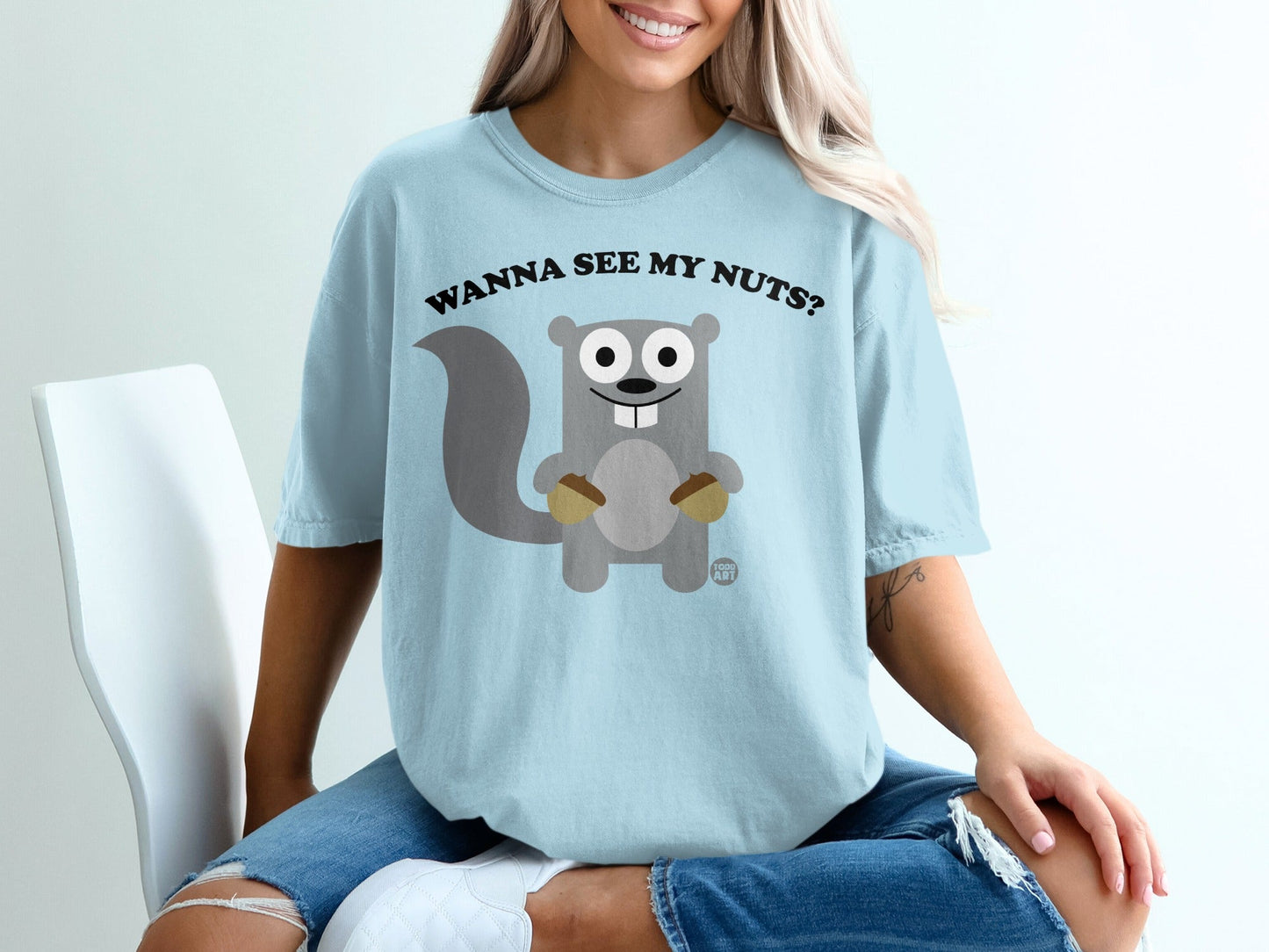 Light blue t-shirt with cartoon squirrel holding acorns and text "Wanna see my nuts?".