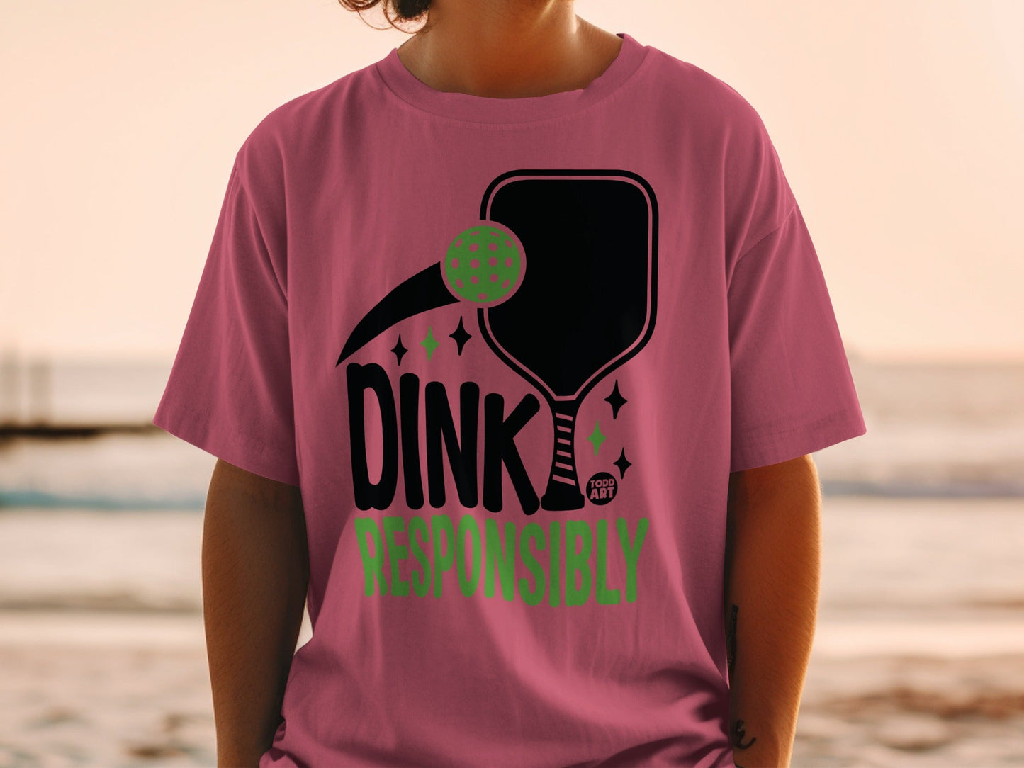 Pink t-shirt with "DINK RESPONSIBLY" text and pickleball graphic.