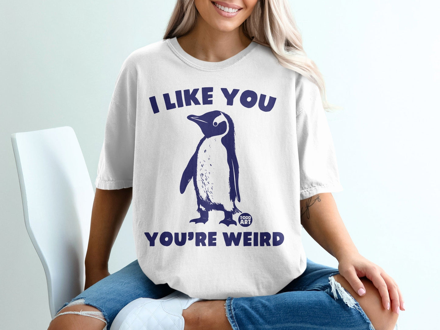 White t-shirt with navy penguin graphic and text "I LIKE YOU YOU'RE WEIRD".