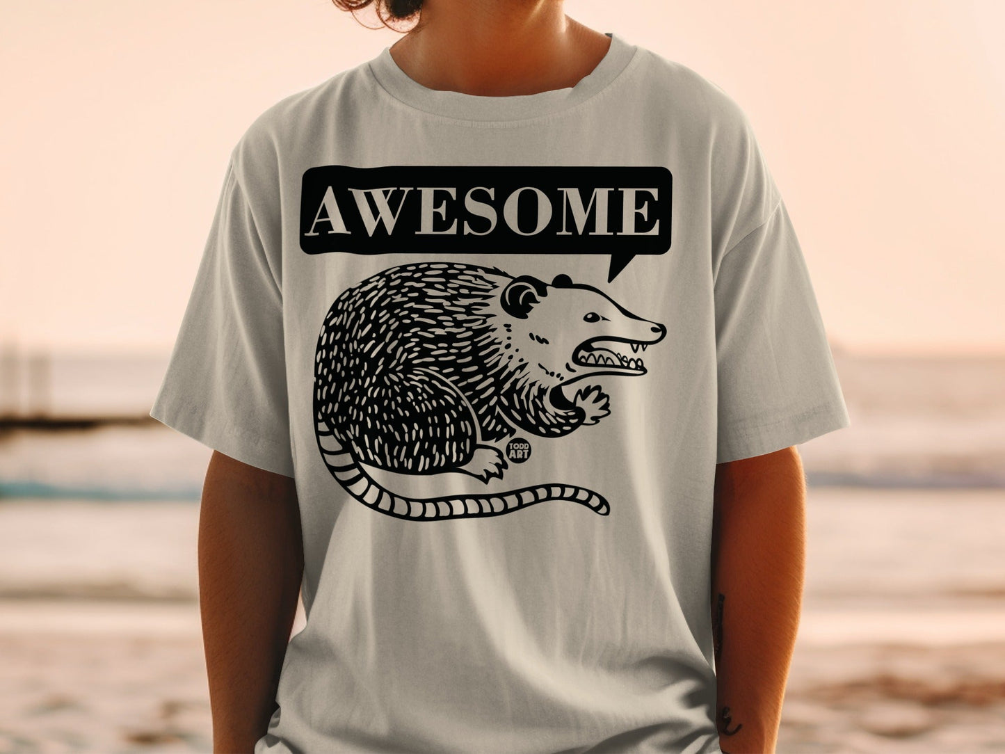 Gray t-shirt with black illustration of a possum in a speech bubble saying "AWESOME".
