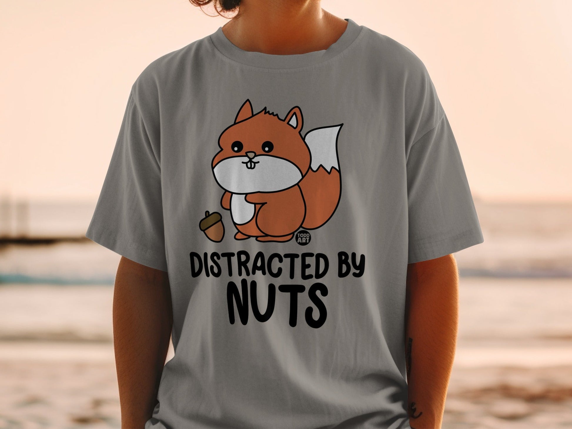Gray t-shirt with a cartoon squirrel holding an acorn and the text "DISTRACTED BY NUTS".